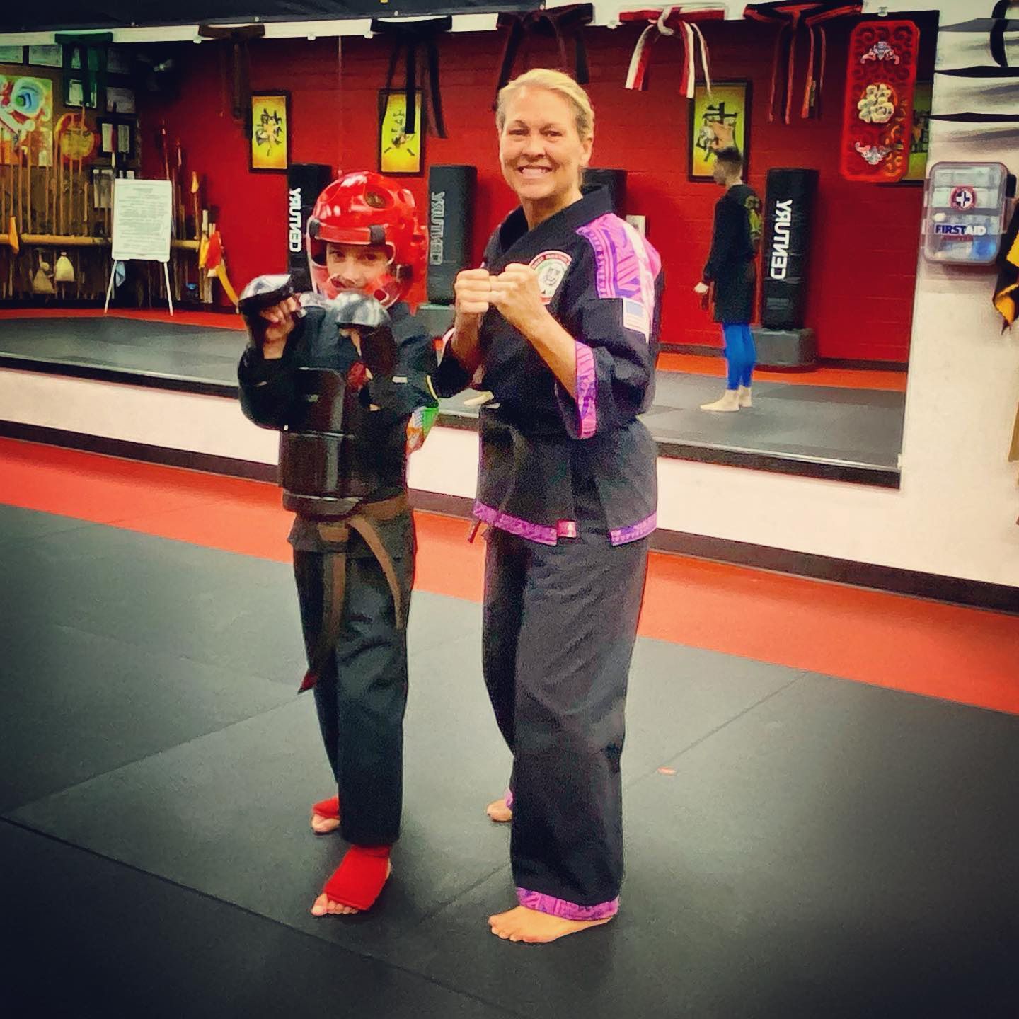 A woman stands next to a young boy in a martial arts gym