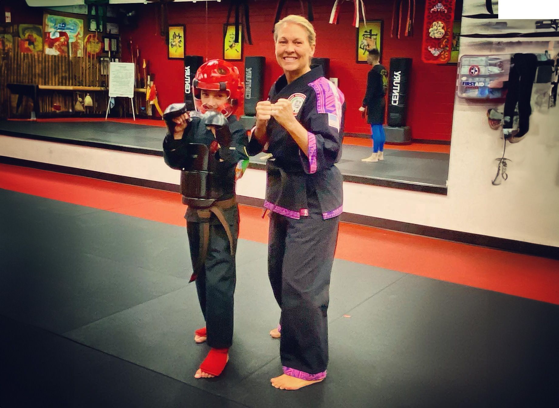 A woman is standing next to a young boy in a martial arts gym.