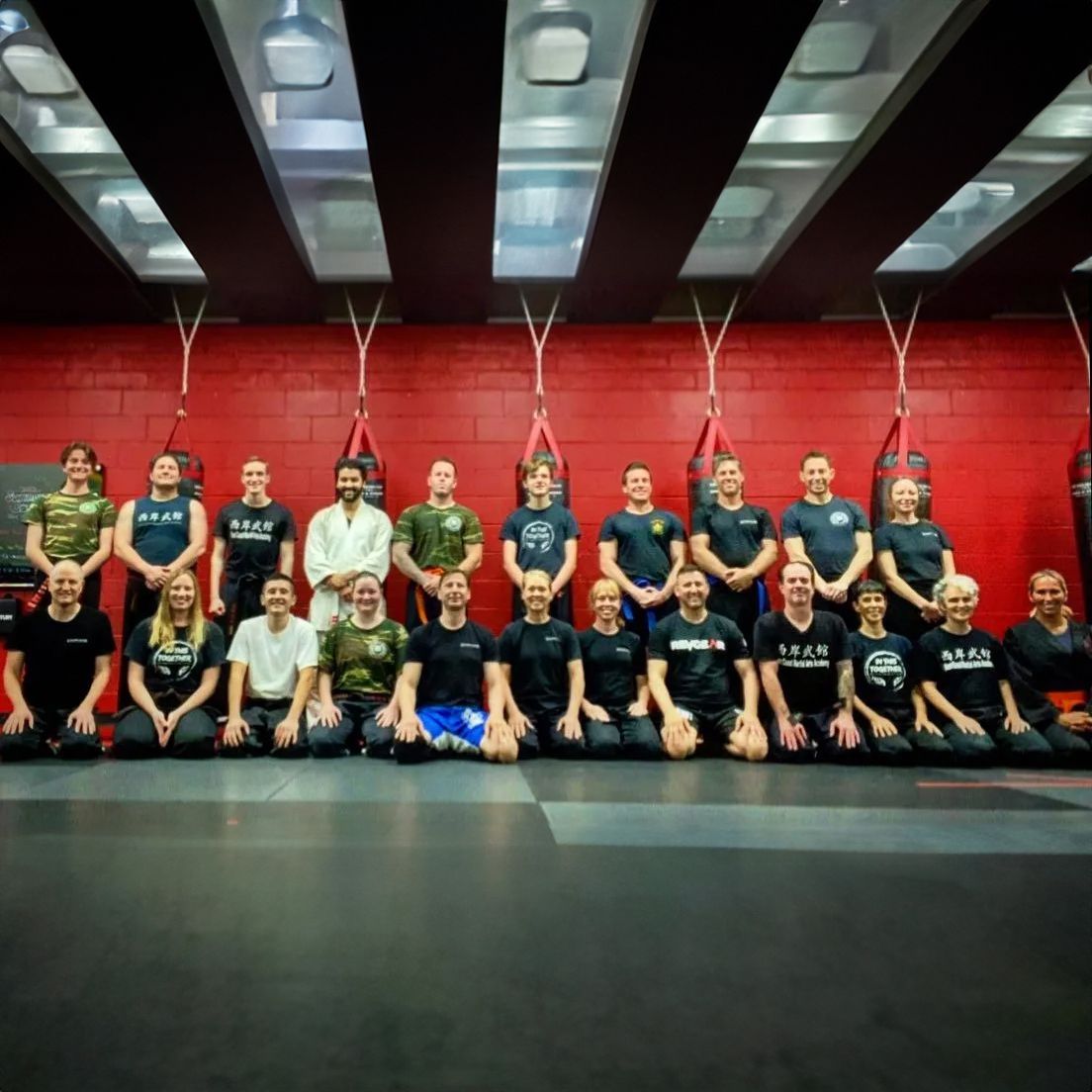 A group of people posing for a picture in a gym with a red wall