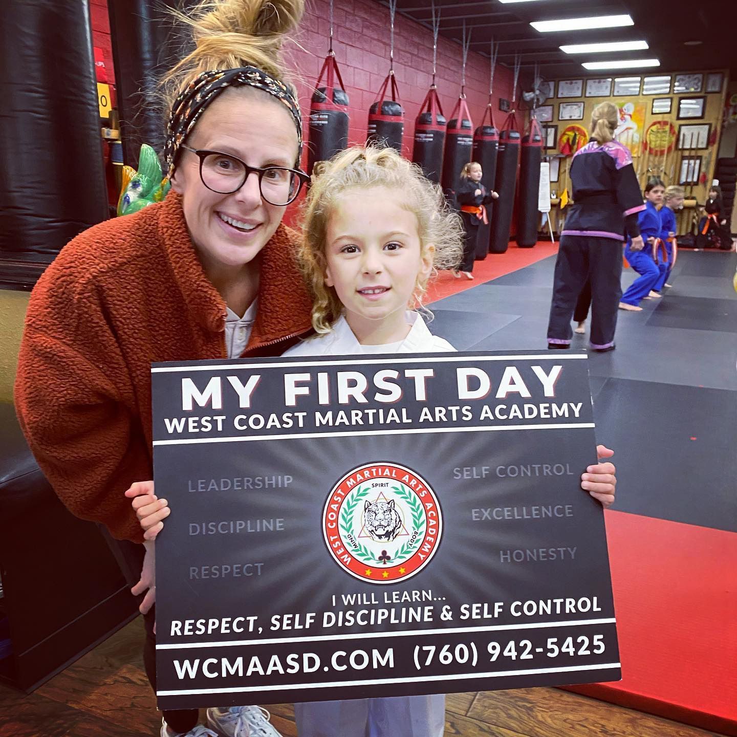 A woman is holding a sign that says my first day west coast martial arts academy