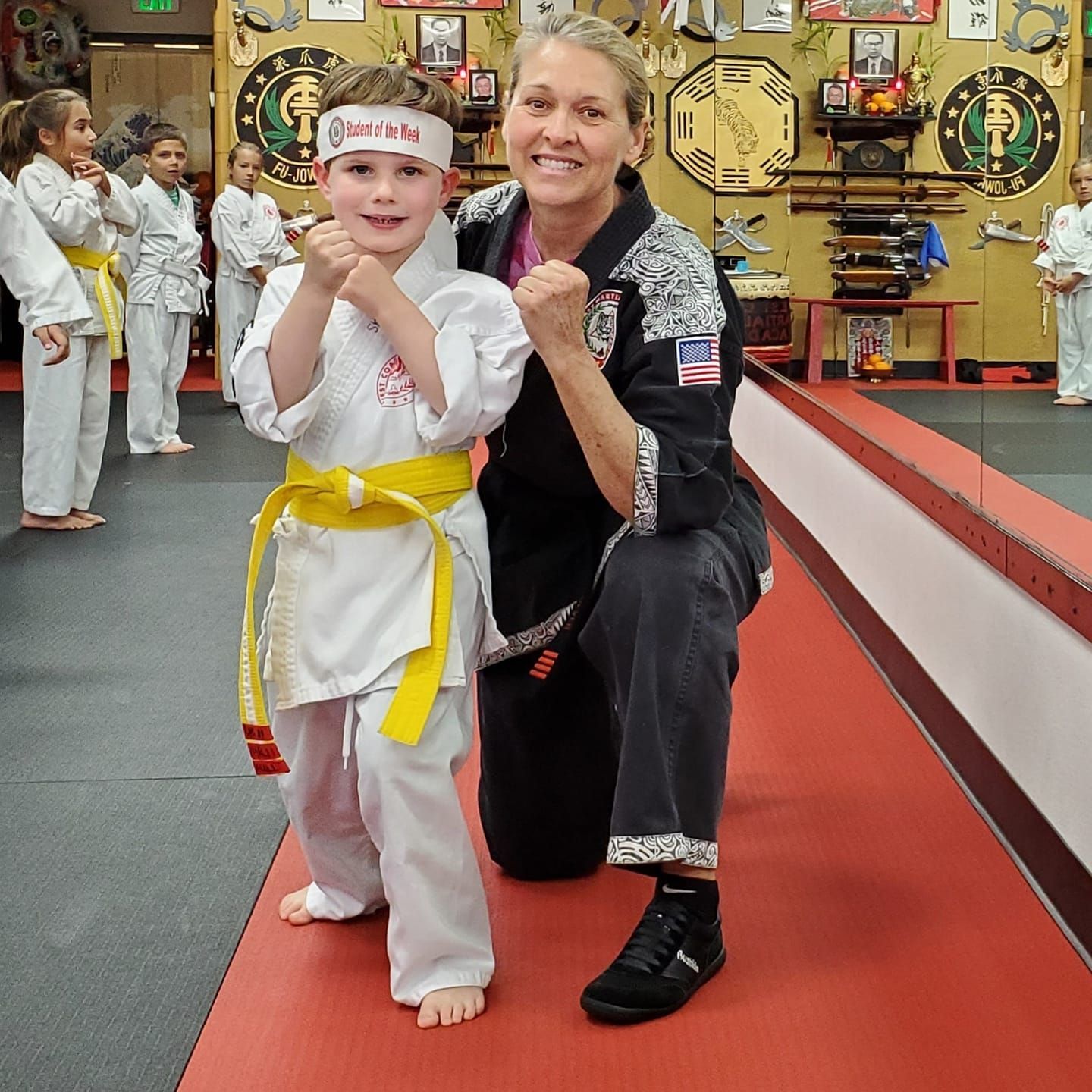 A woman kneeling next to a young boy wearing a headband that says karate on it