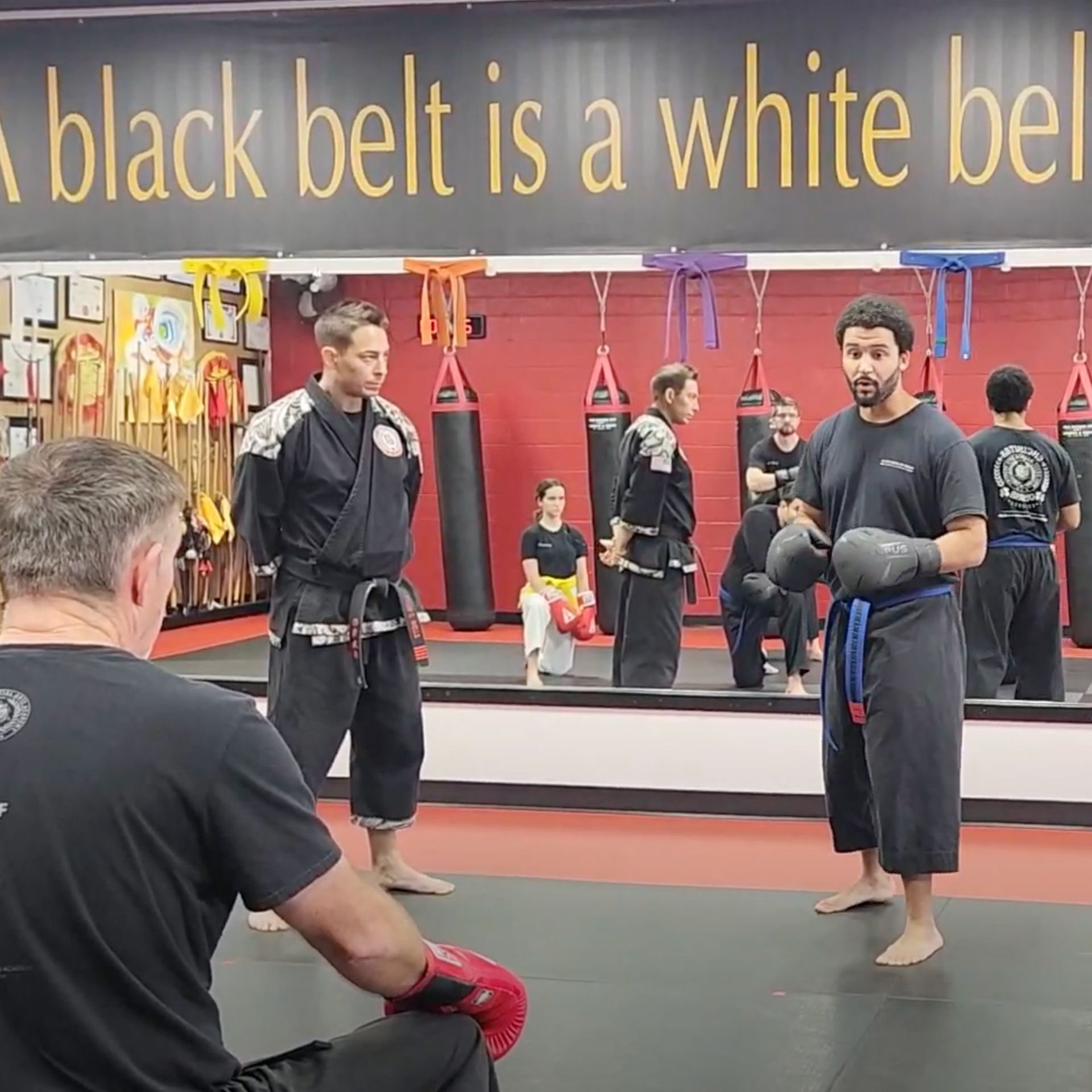 A man is taking a picture of a group of people in a gym under a sign that says black belt is a white belt