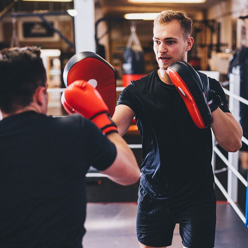 Two men are boxing in a gym and one is wearing red gloves