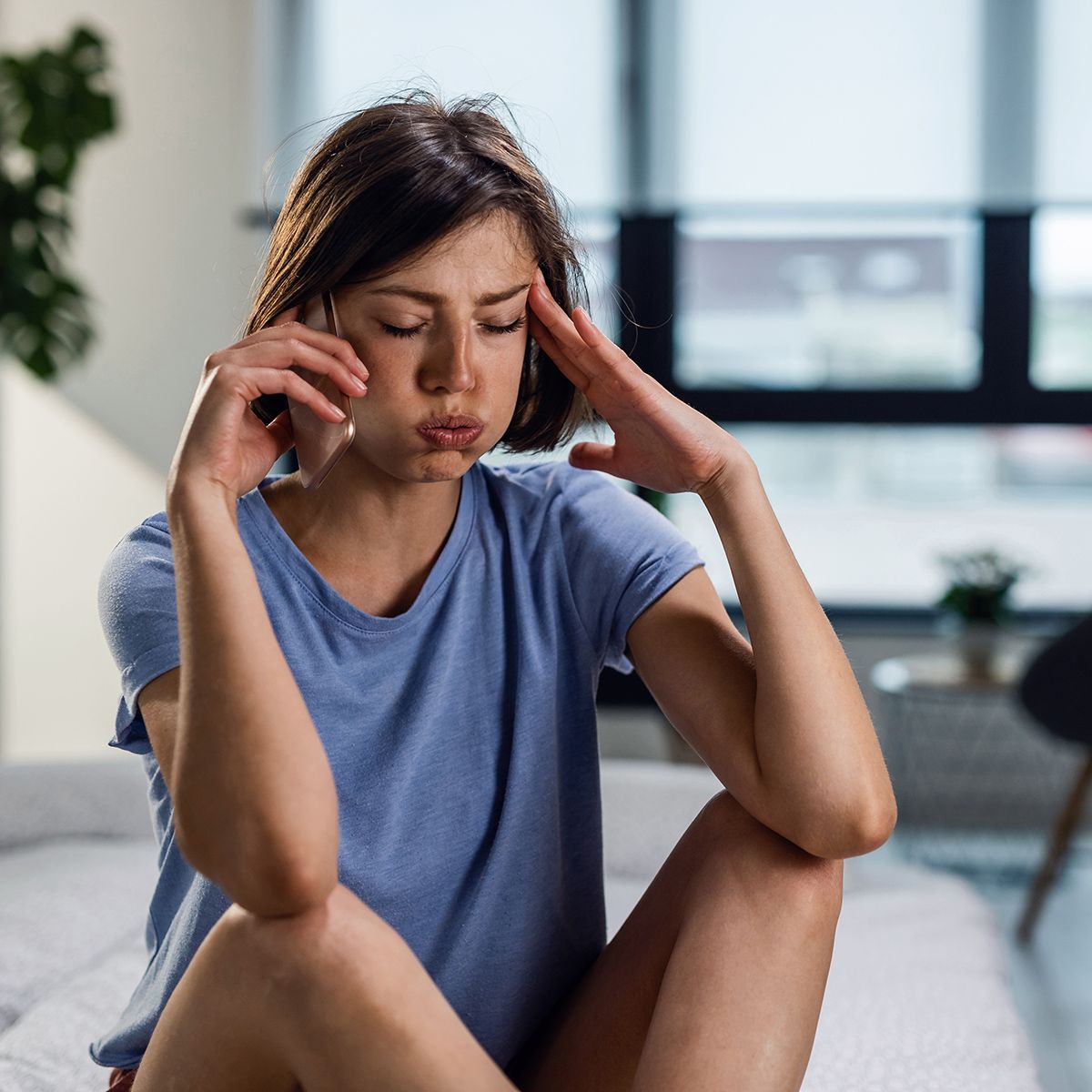 A woman is sitting on a bed with her head in her hands.