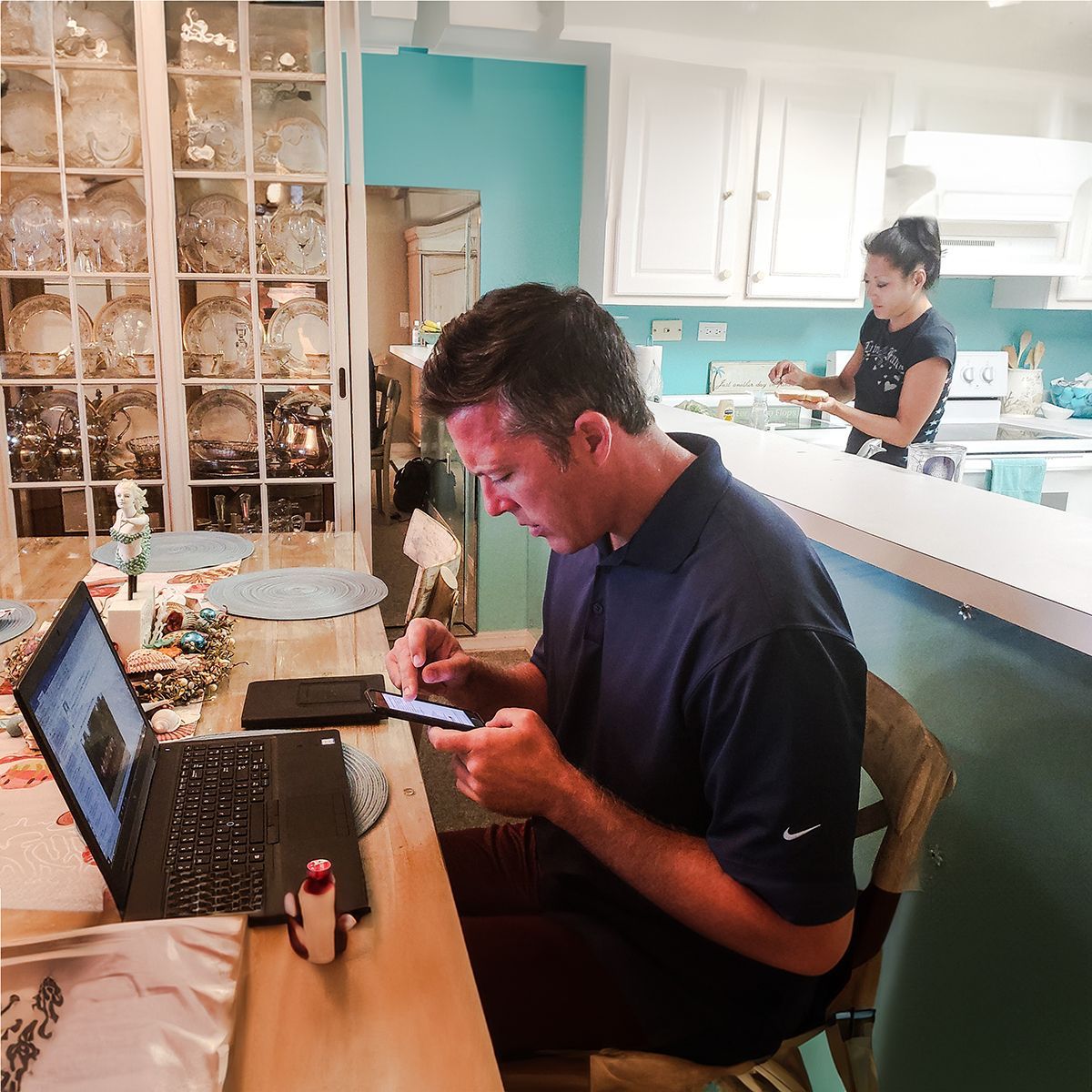 A man sits at a table with a laptop and a cell phone