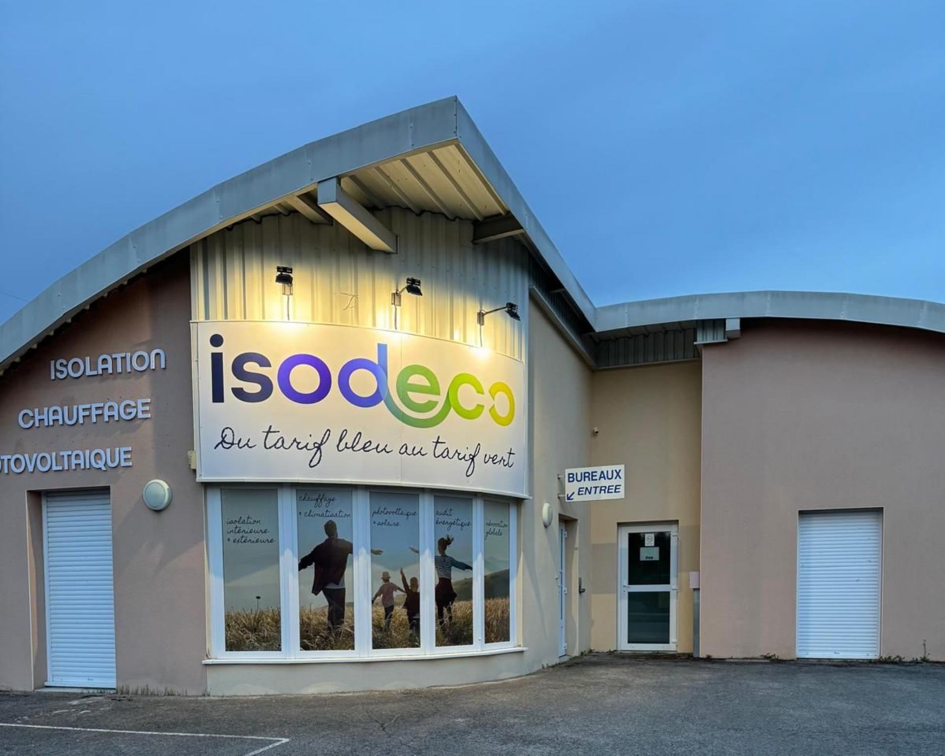 Extérieur du bâtiment commercial d'Isodeco, avec une grande enseigne et des graphismes sur les vitrines montrant des personnes dans un champ.
