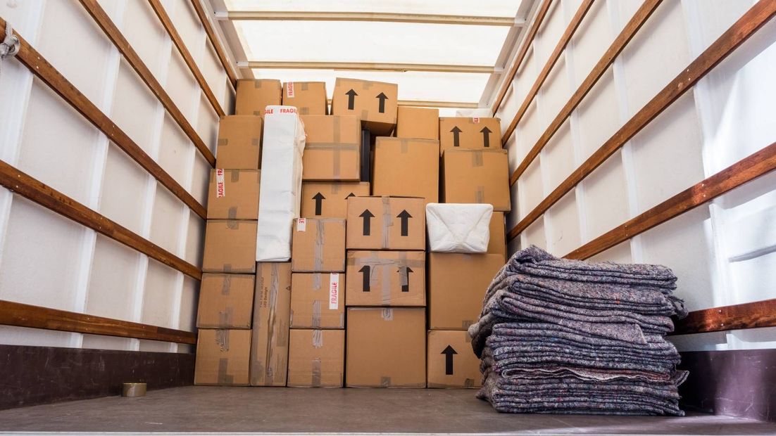 Boxes stacked in a moving truck, some with arrow markings, and a pile of blankets.