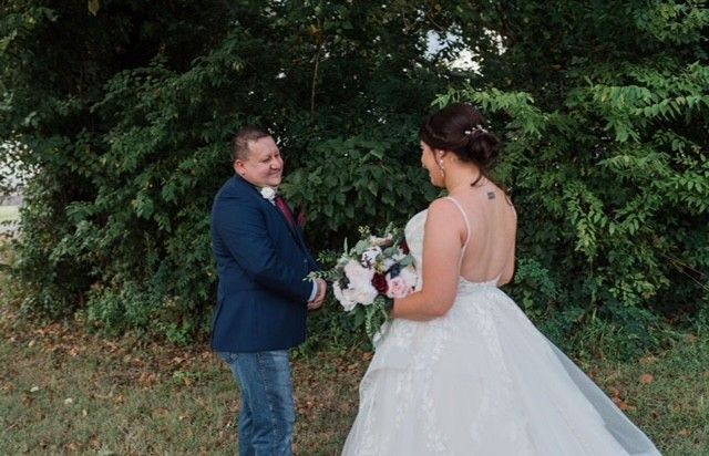 A bride and groom are standing next to each other in a field.