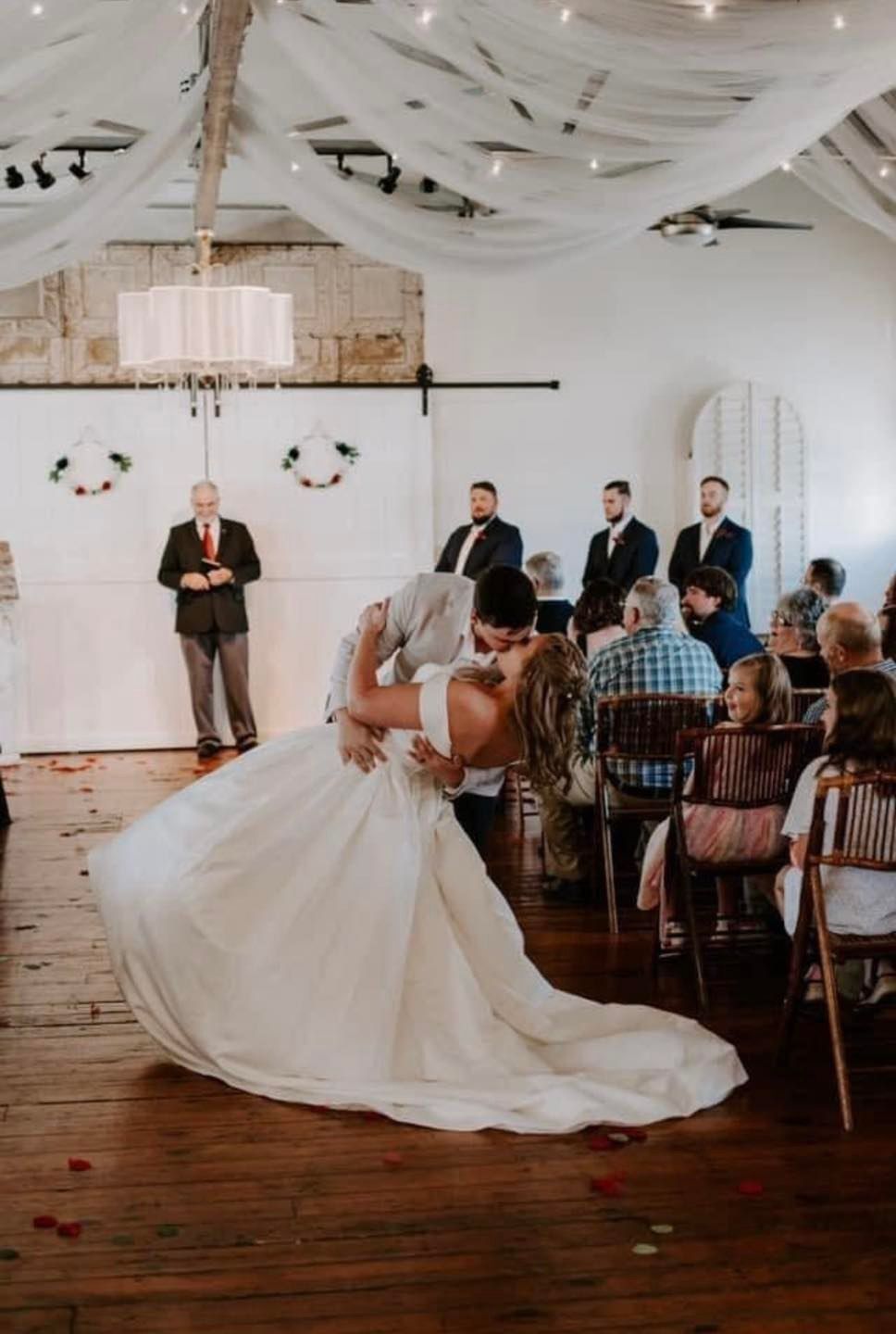 A bride and groom are kissing during their wedding ceremony in front of their wedding guests.