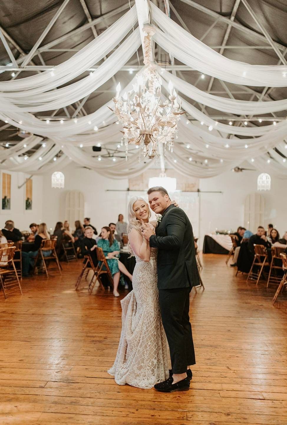 A bride and groom are dancing in a large room at their wedding reception.