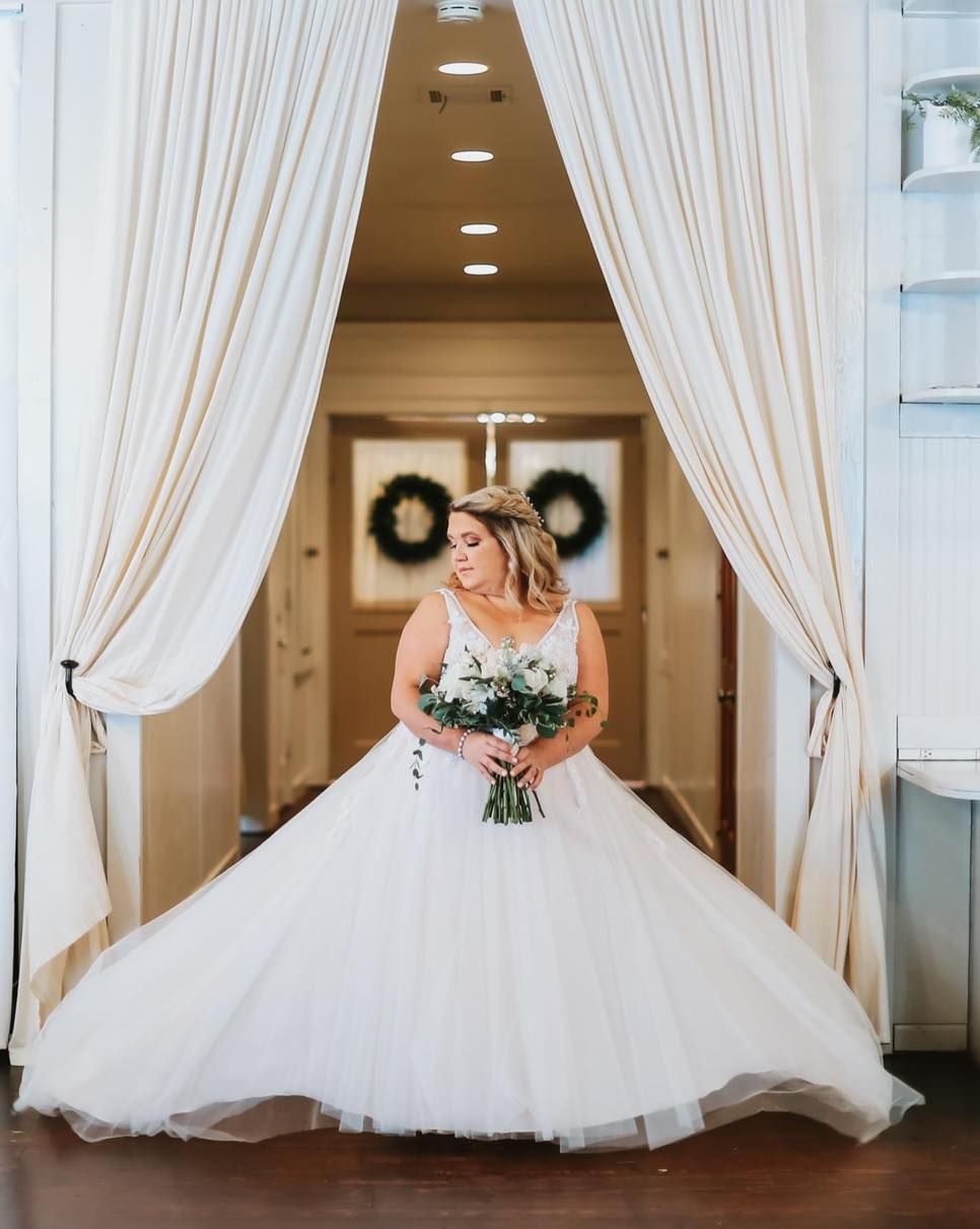A bride in a wedding dress is standing in a hallway holding a bouquet of flowers.