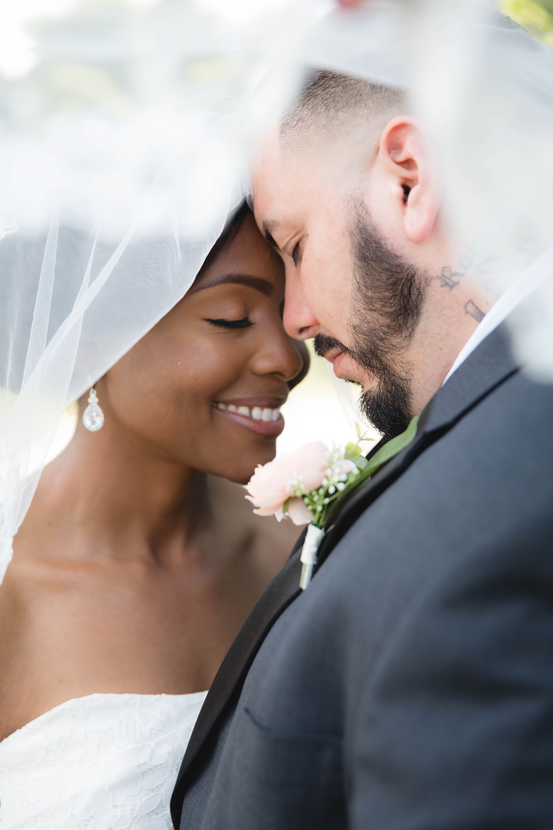 A bride and groom are touching their foreheads under a veil.