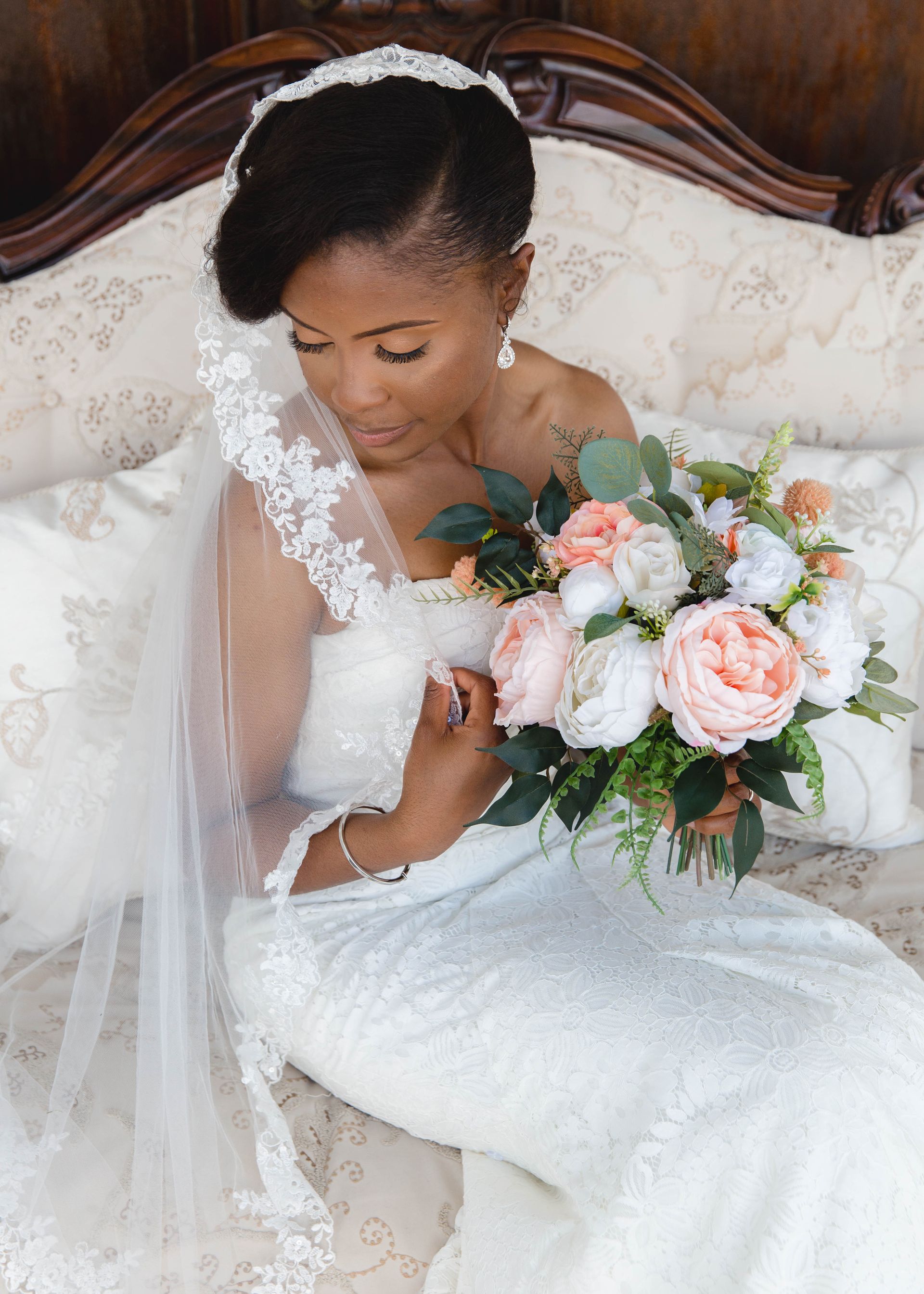A bride in a wedding dress is sitting on a bed holding a bouquet of flowers.