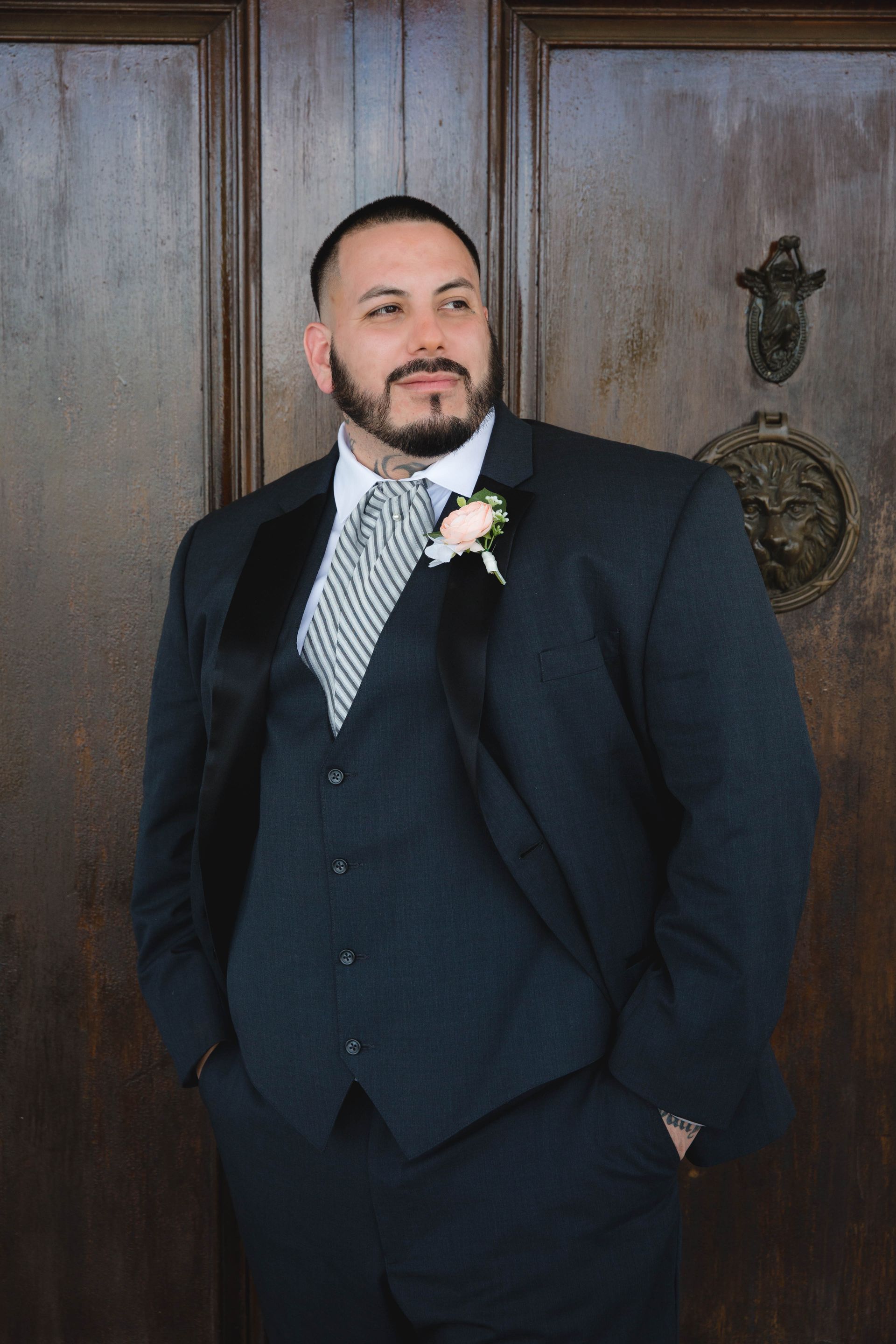 A man in a suit and tie is standing in front of a wooden door.