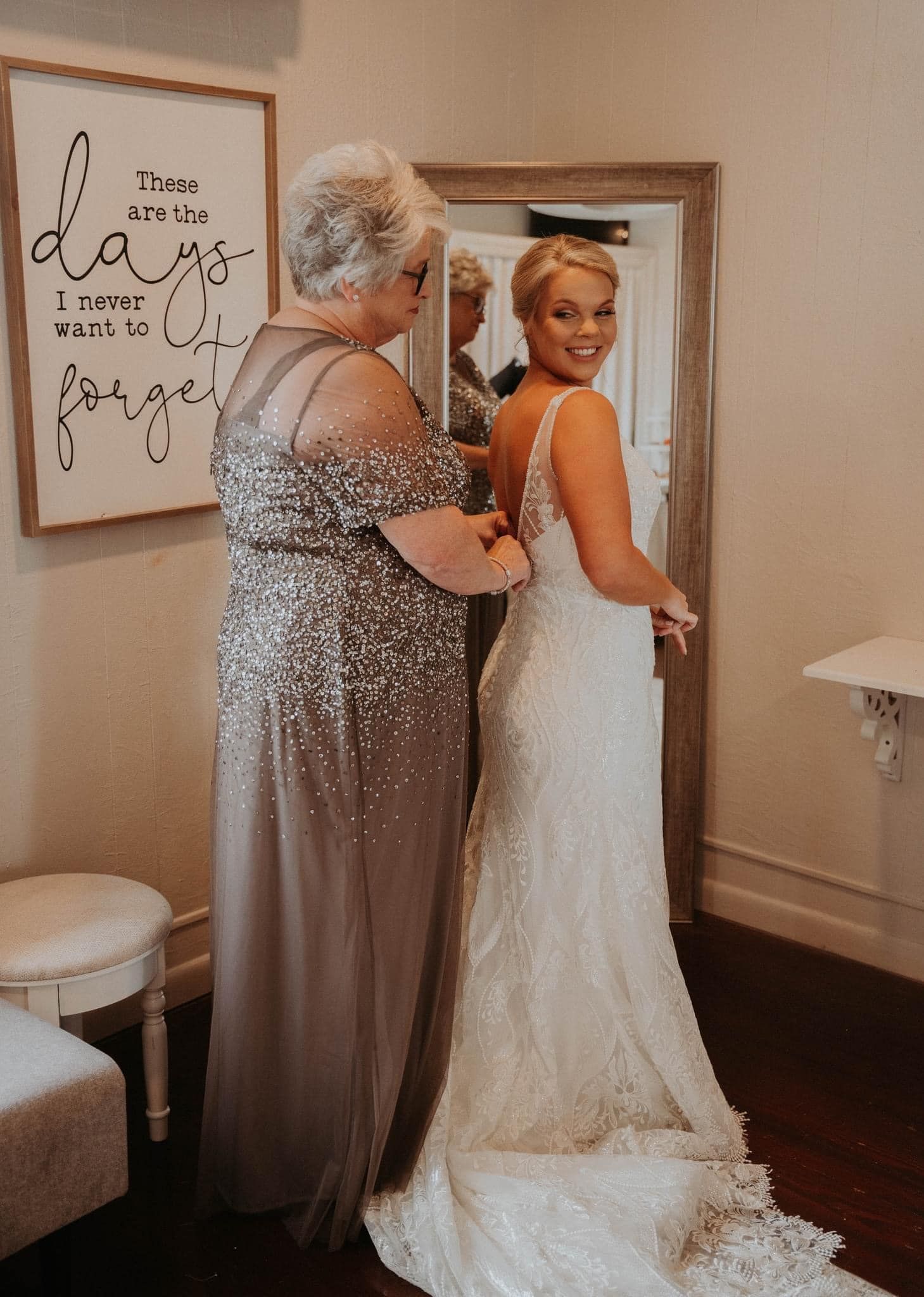 A woman is helping a bride get ready for her wedding in front of a mirror.