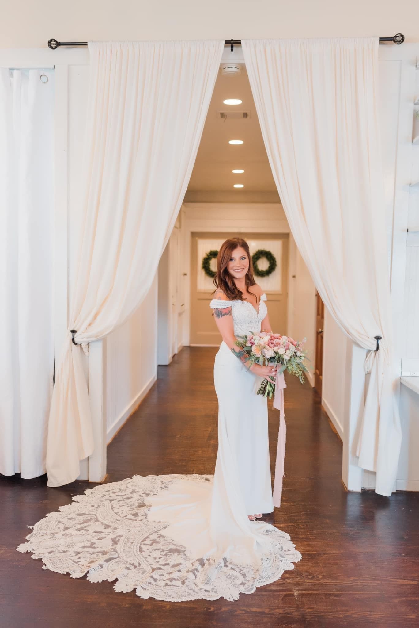 A bride in a wedding dress is standing in a hallway holding a bouquet of flowers.