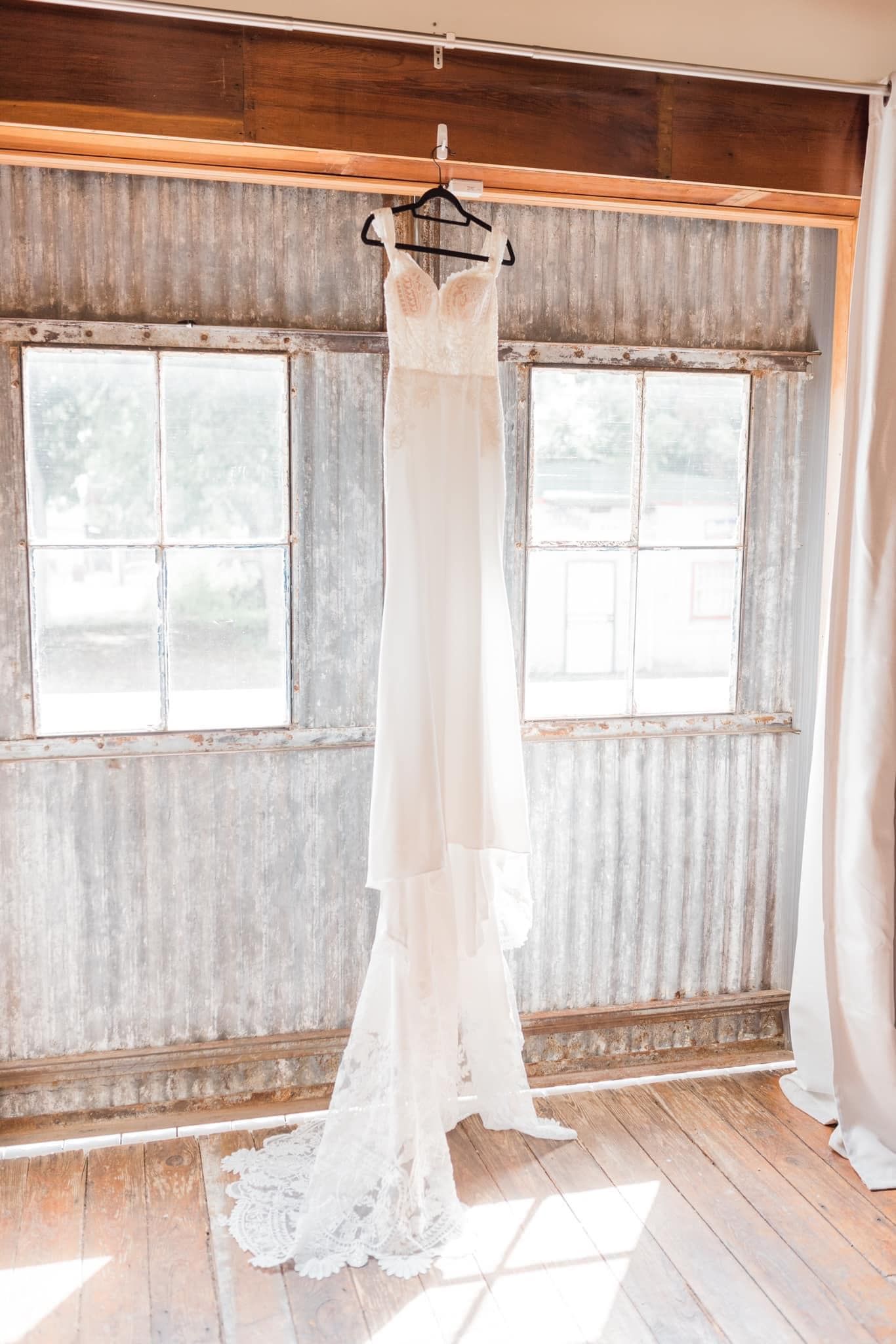 A wedding dress is hanging on a hanger in a room.