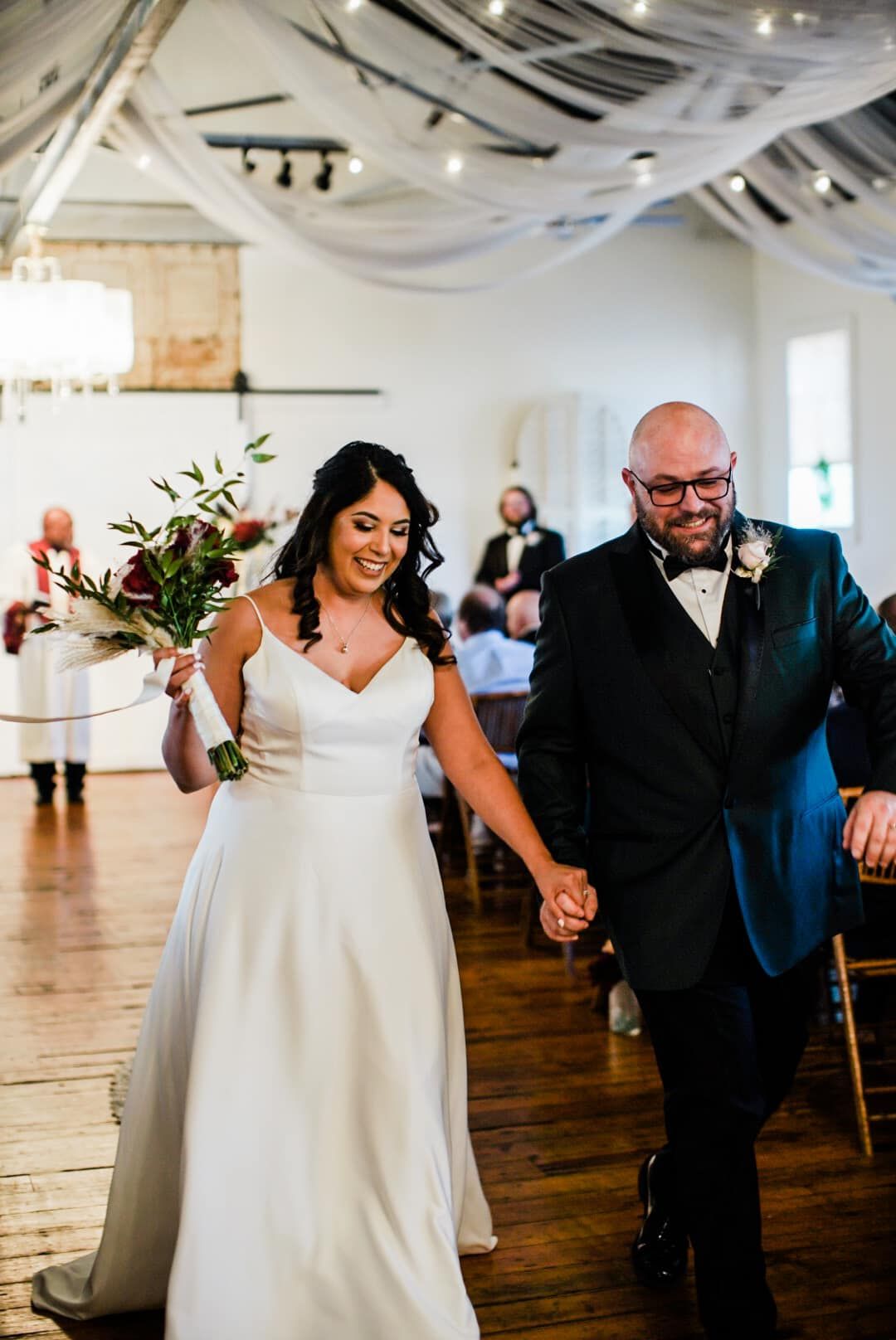 A bride and groom are walking down the aisle holding hands.
