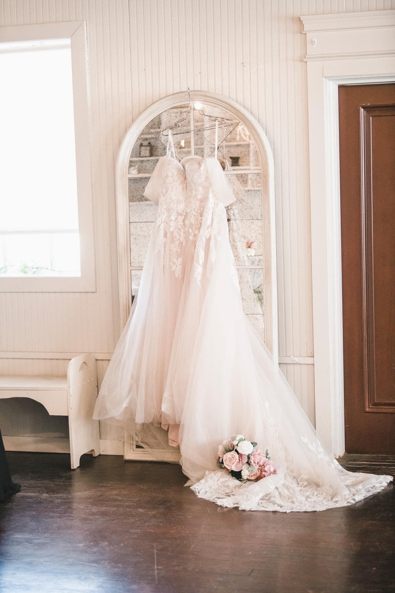 A bride 's wedding dress is hanging on a hanger in front of a mirror.