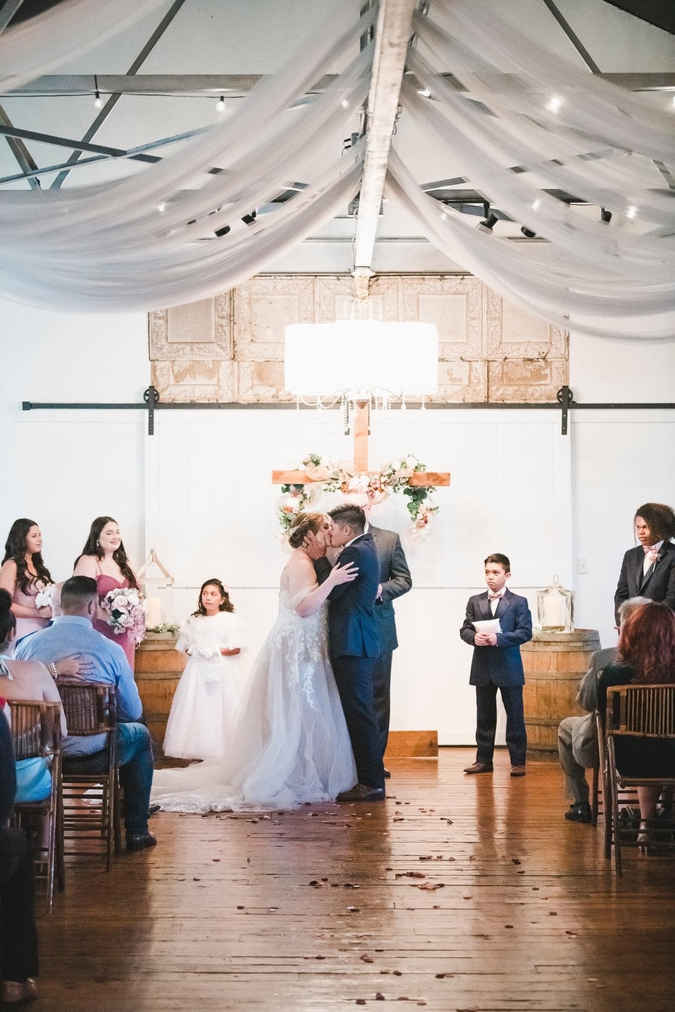 A bride and groom are kissing during their wedding ceremony in front of their wedding guests.