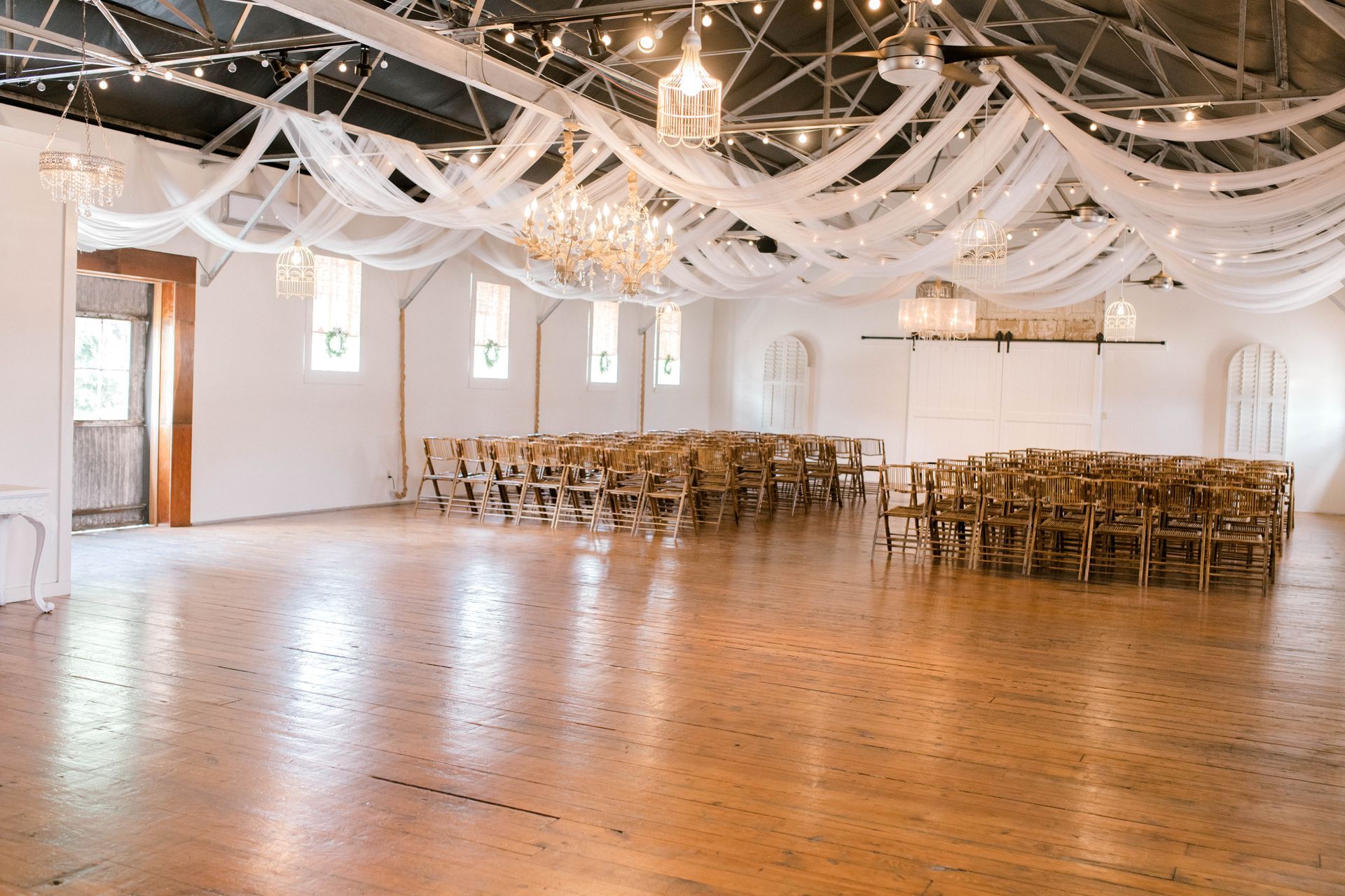 A large empty room with wooden floors and rows of chairs.