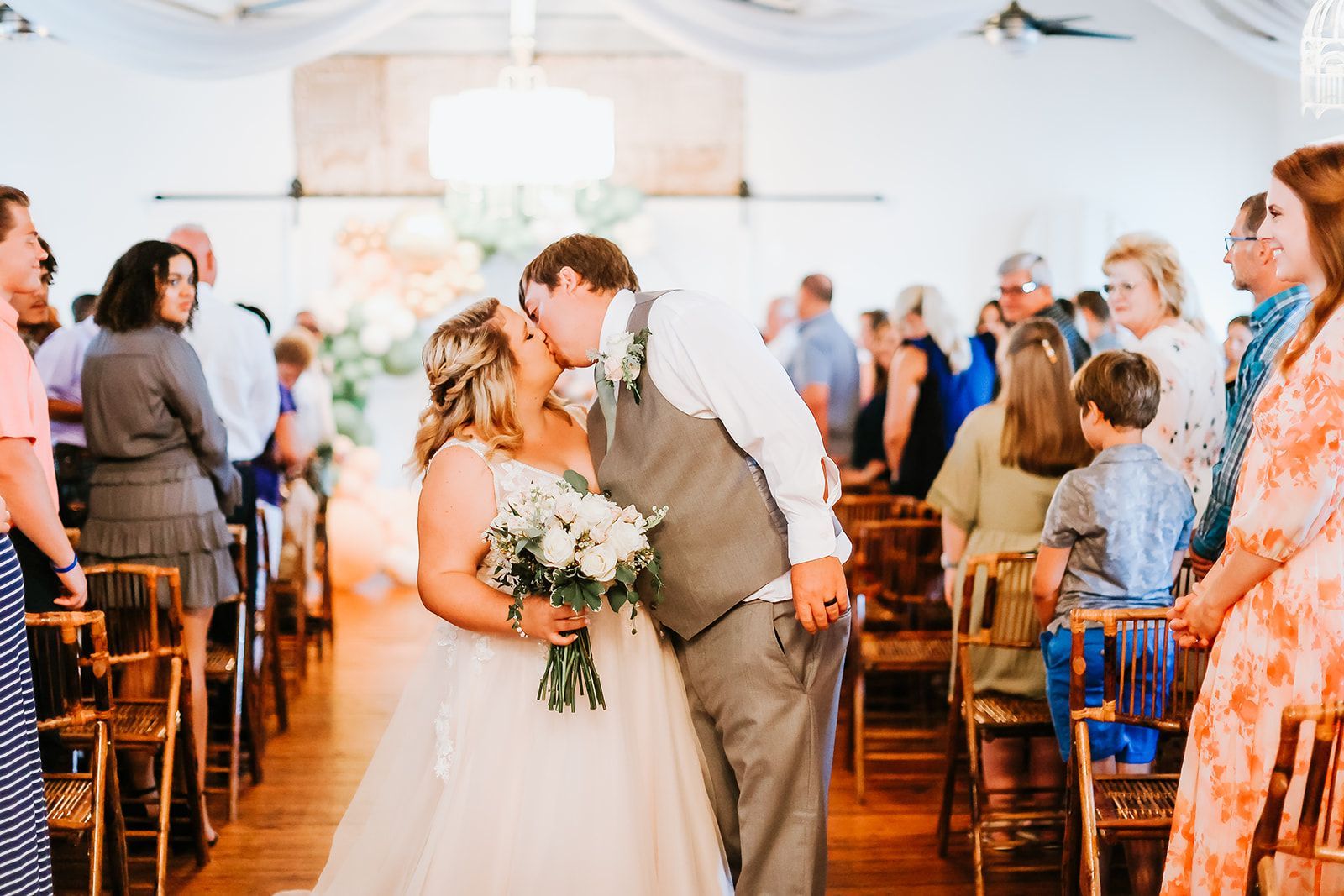 A bride and groom kissing at their wedding ceremony in front of their wedding guests.