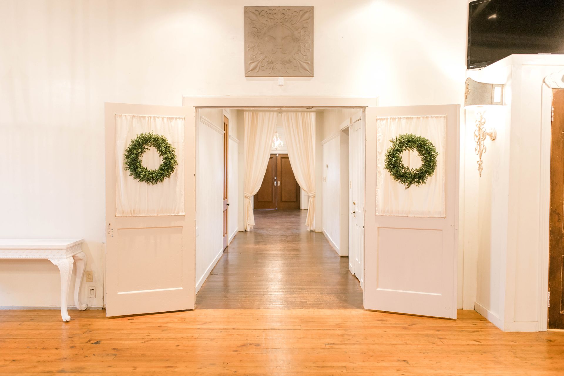 A hallway with a wooden floor and white doors with wreaths on them.