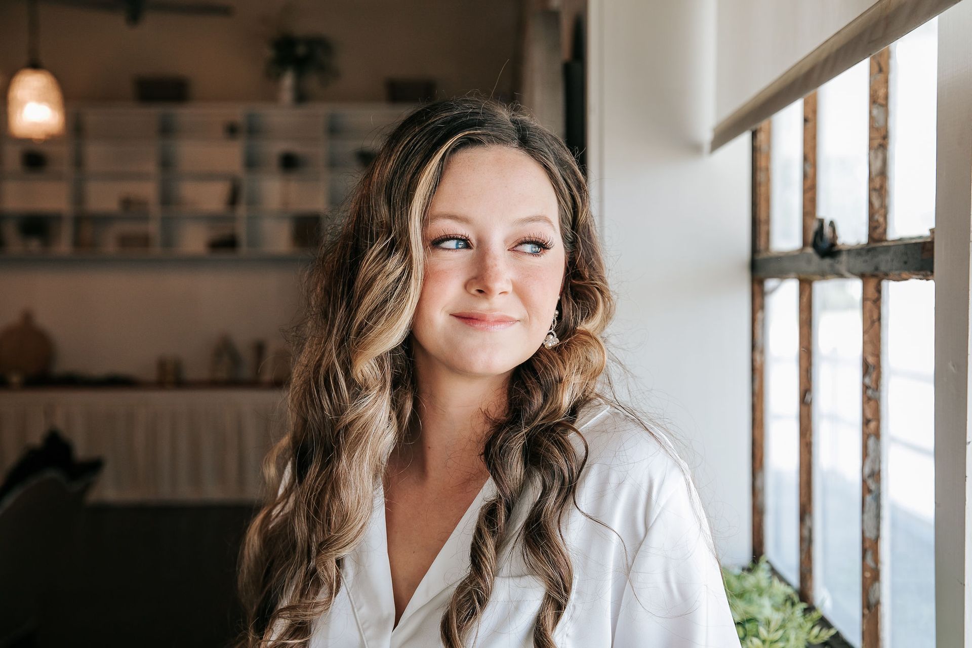 A woman in a white robe is standing in front of a window.