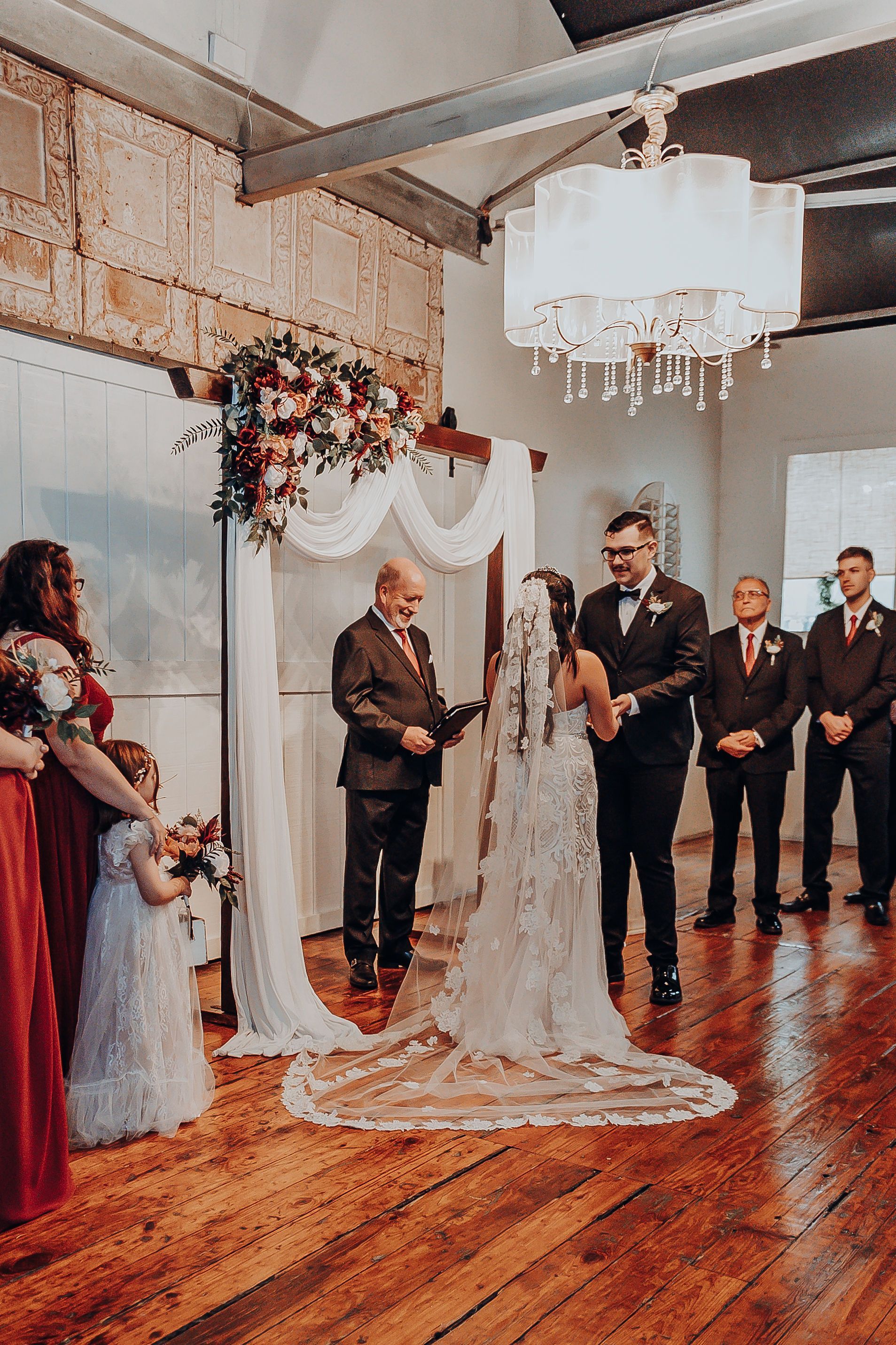 A bride and groom are getting married in a room with a wooden floor.