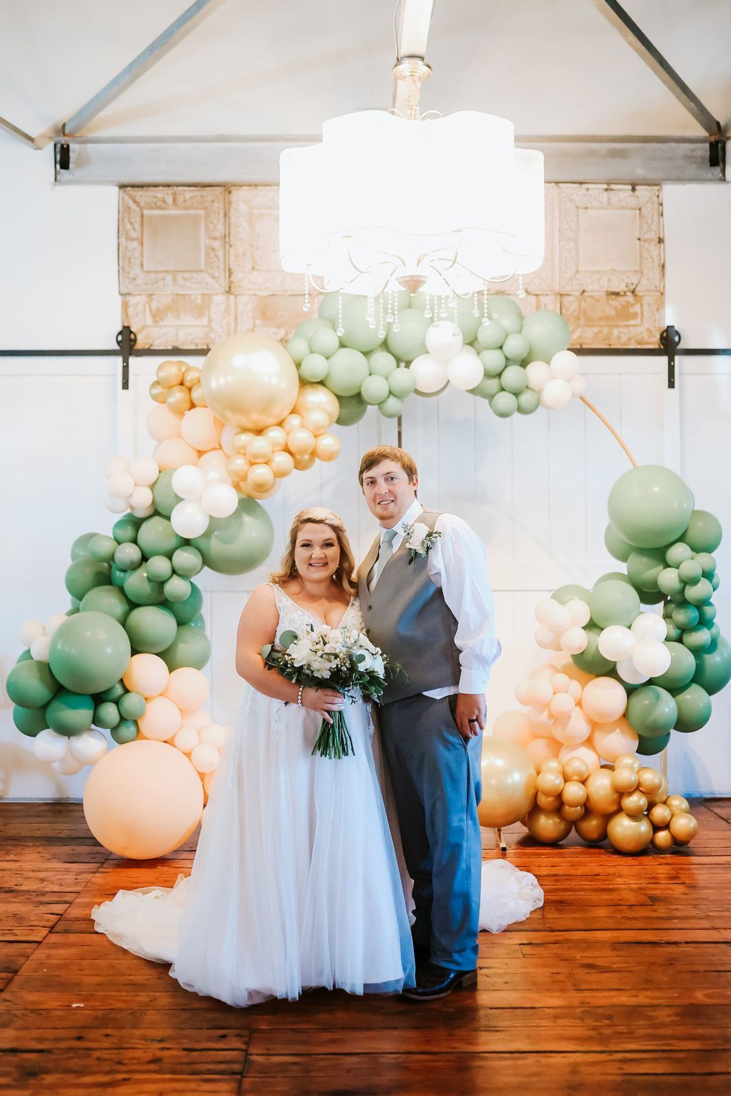 A bride and groom are posing for a picture in front of a balloon arch.