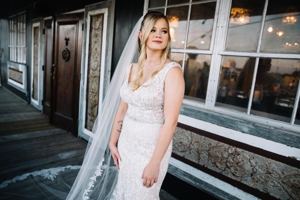 A bride in a wedding dress and veil is standing in front of a building.