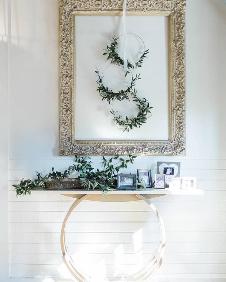 A picture frame with a wreath on it is hanging on a wall above a table.