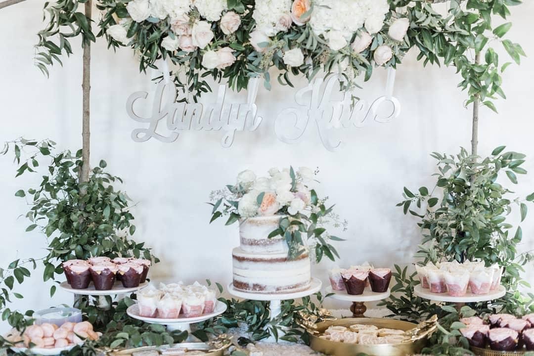 A dessert table with a cake , cupcakes , and flowers.