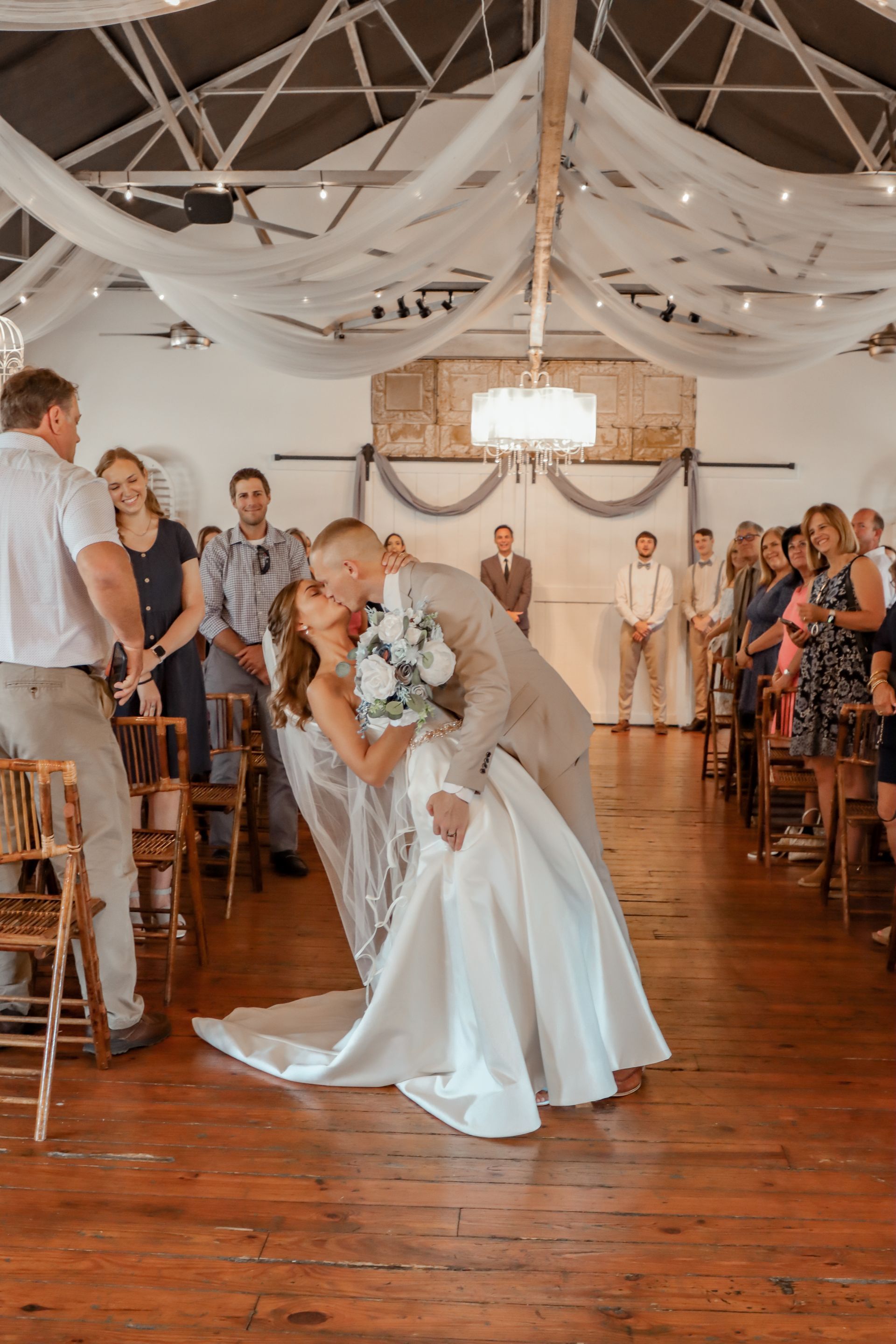 A bride and groom kissing at their wedding ceremony in front of a crowd.