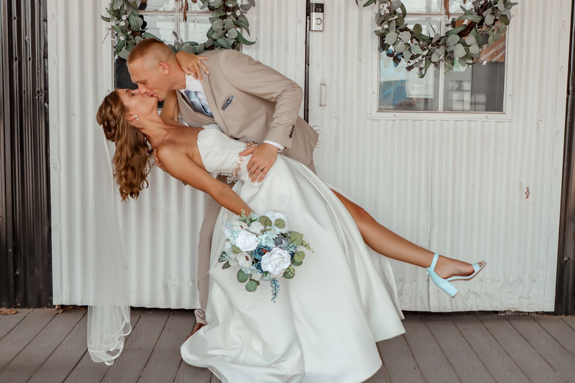 A bride and groom are kissing in front of a white building.