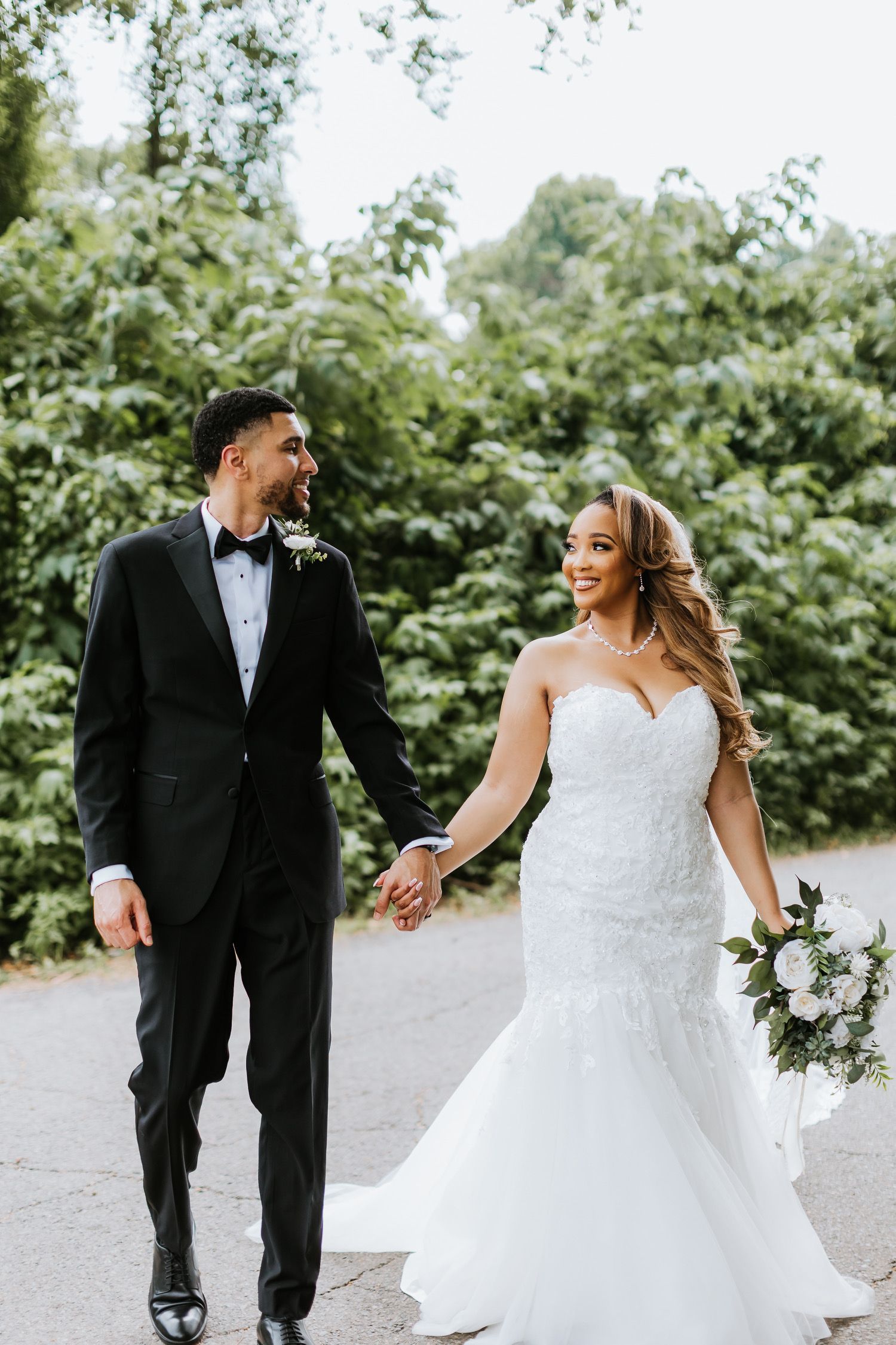 A bride and groom are walking down a road holding hands.