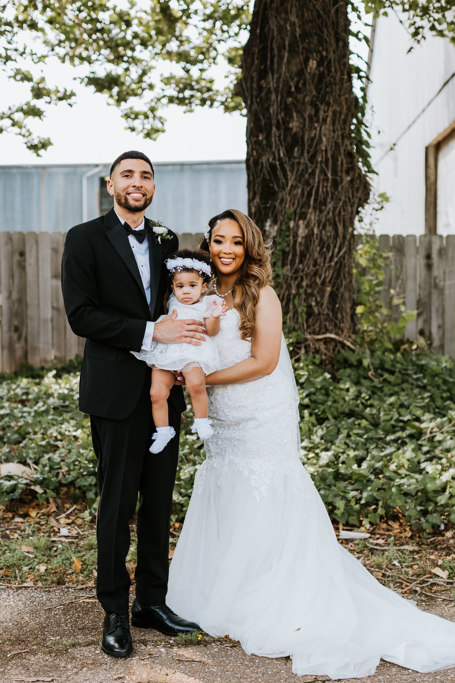 A bride and groom are posing for a picture with their baby girl.