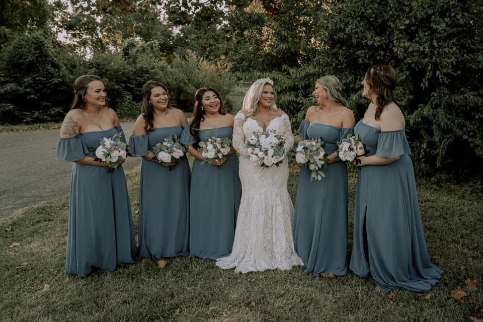 A bride and her bridesmaids are posing for a picture in the grass.