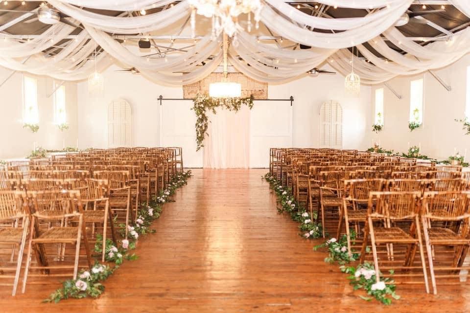 Rows of wooden folding chairs are lined up in a large room for a wedding ceremony.