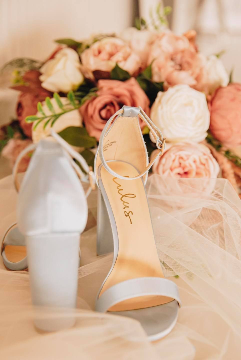 A pair of wedding shoes sitting on top of a table next to a bouquet of flowers.