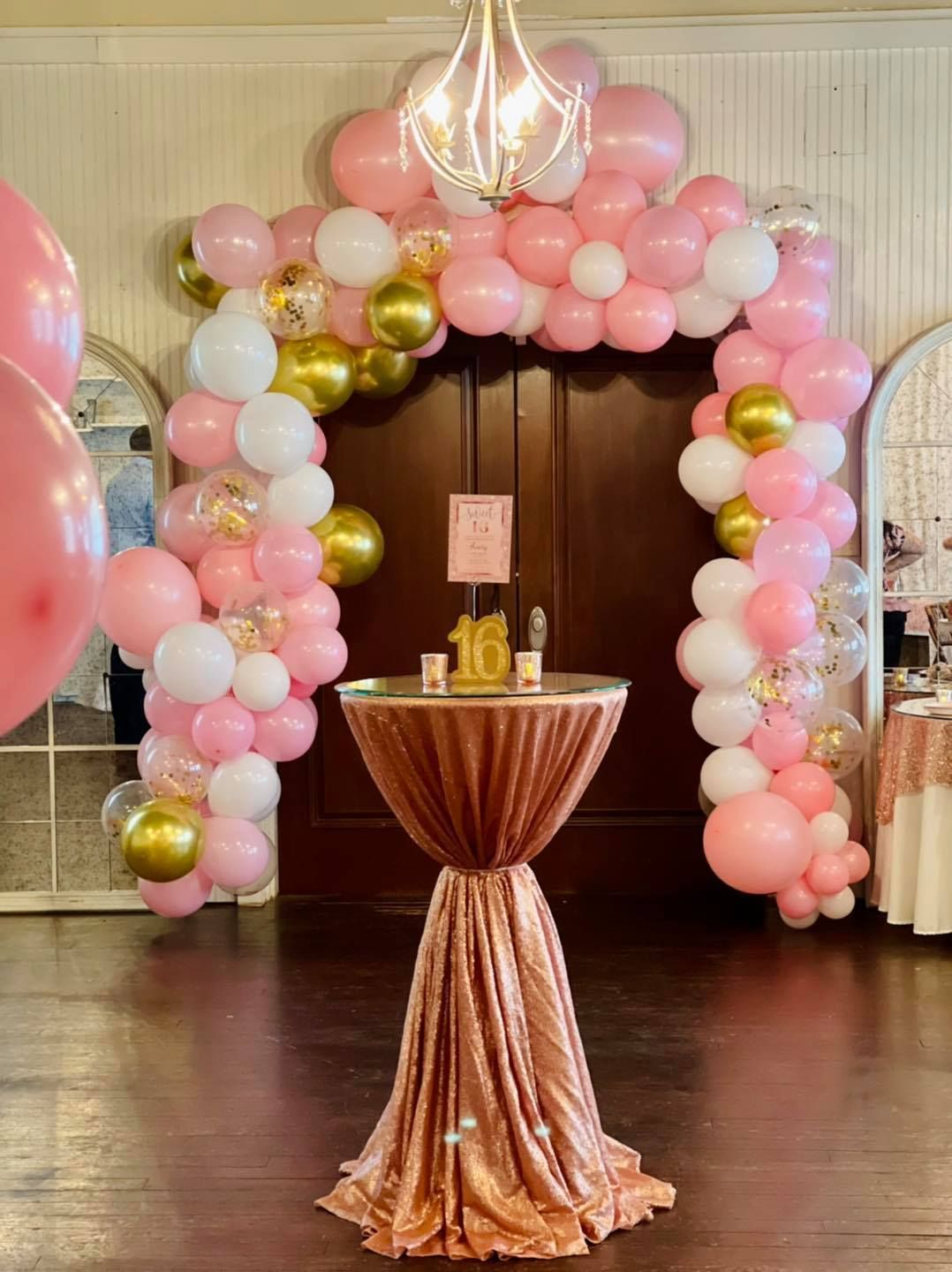 A room decorated with pink , white and gold balloons and a table.