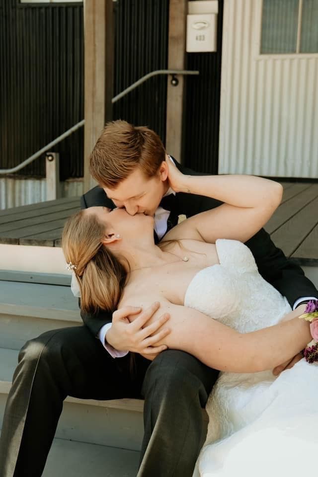 A bride and groom are kissing while sitting on a bench in front of a building.