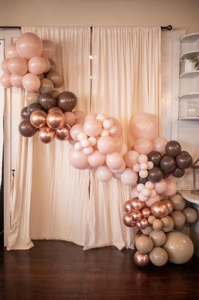 A bunch of balloons are hanging from a curtain in a room.