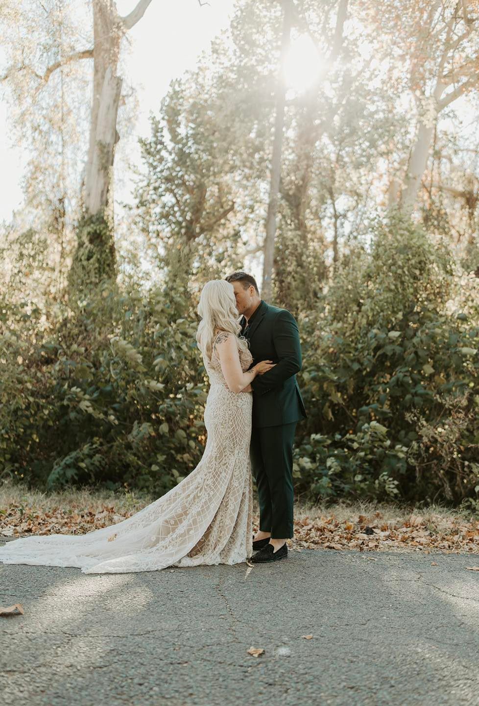 A bride and groom are kissing in front of a forest.