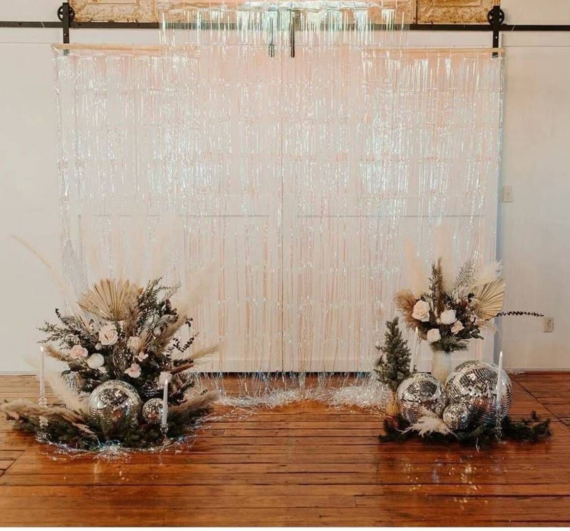 There are two vases of flowers in front of a white curtain.