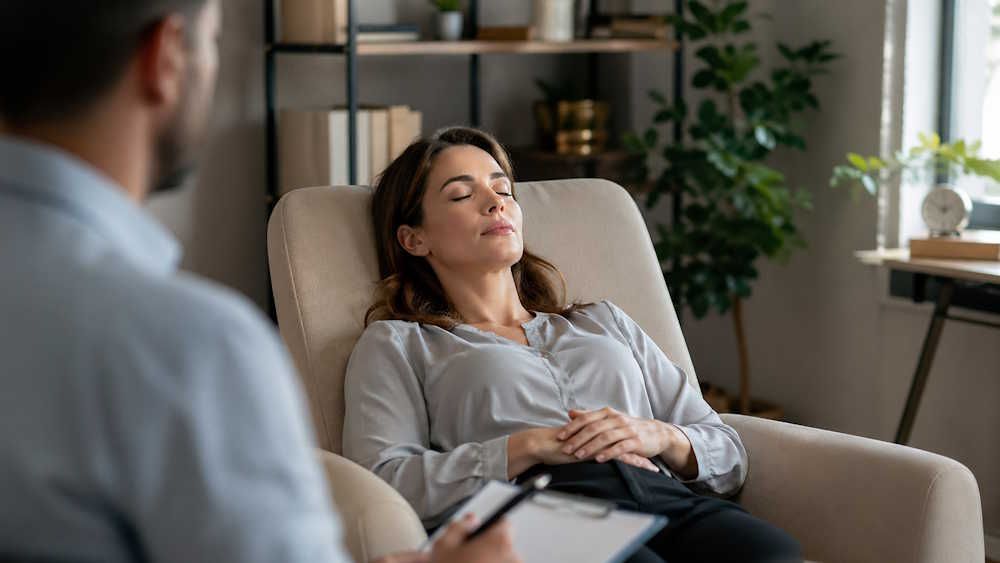 a woman in OKC reclining comfortably in an office, eyes closed, guided by her hypnotherapist