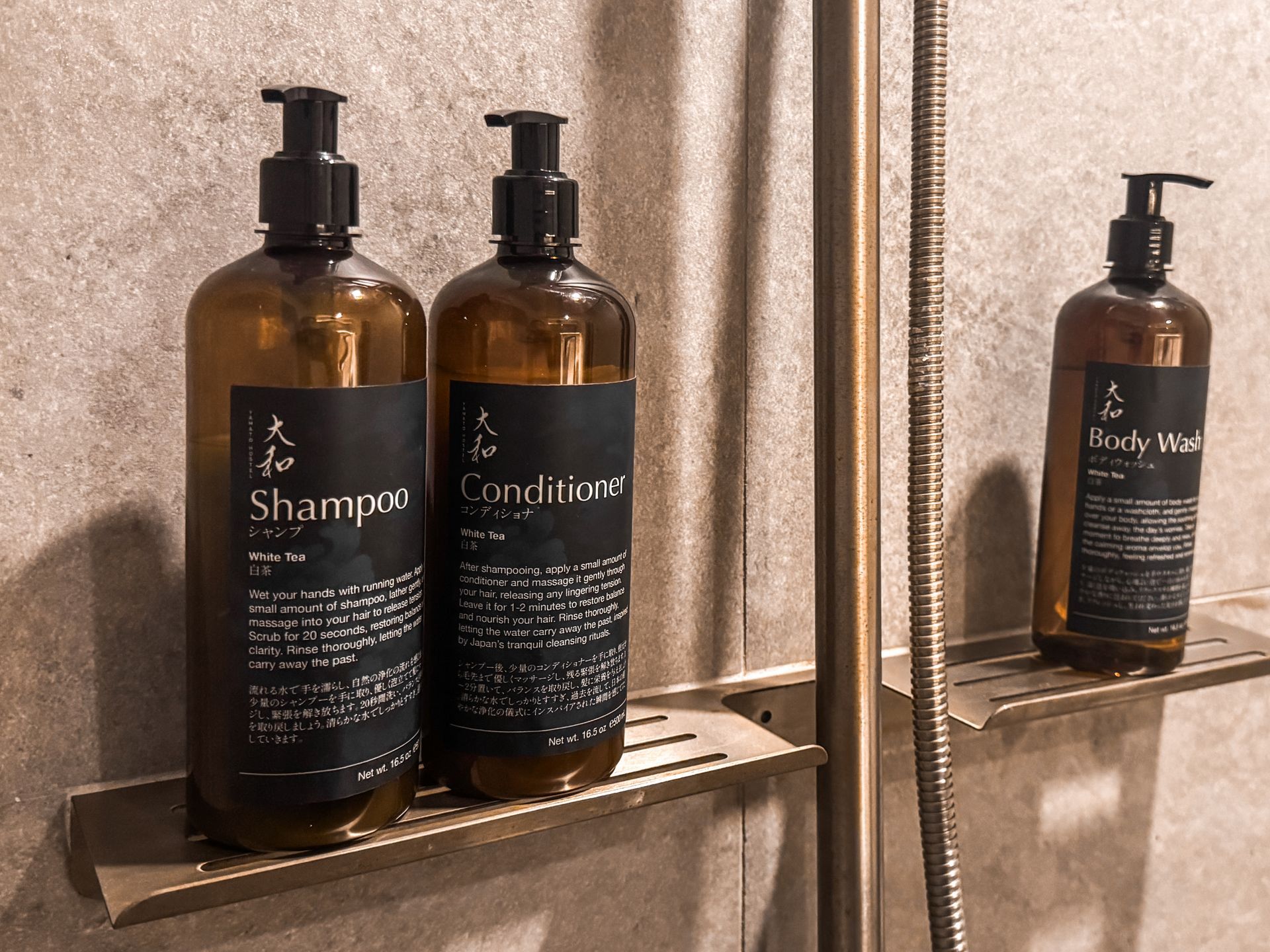 Three bottles of shampoo and conditioner are on a shelf in a bathroom