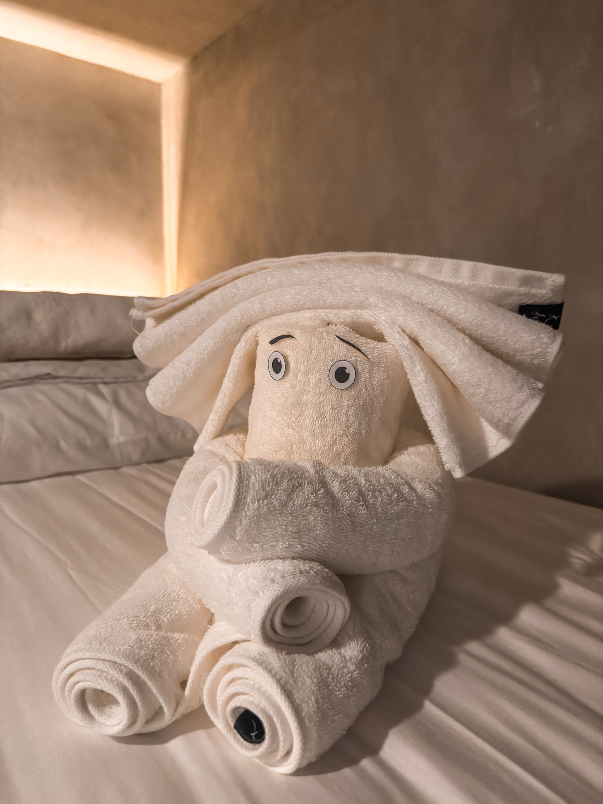 A stuffed animal made out of towels is sitting on a bed.