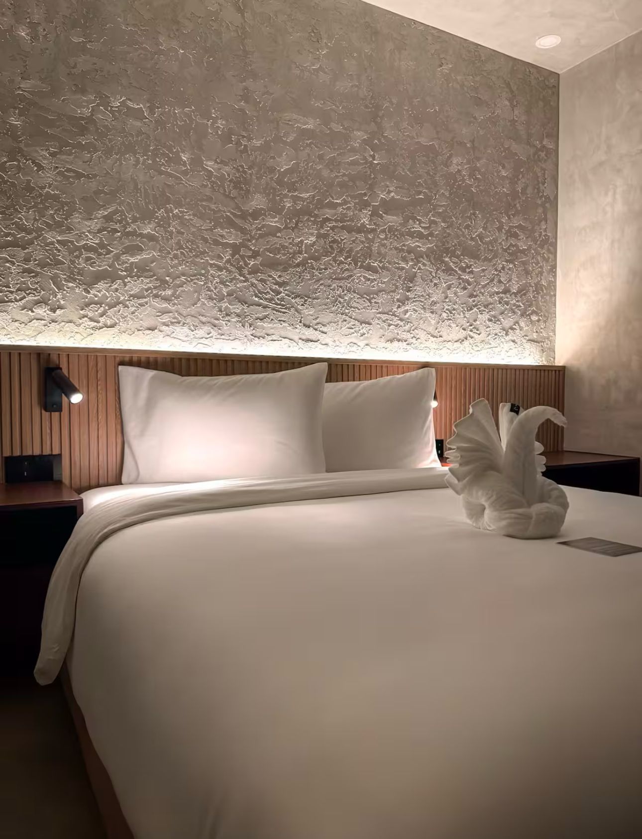 A hotel room with a bed and a swan made out of towels.