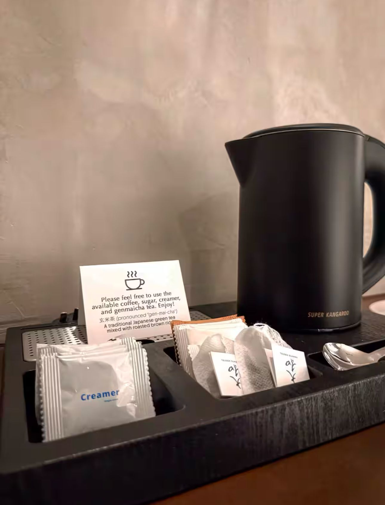 A black kettle is sitting on top of a wooden table next to a tray of tea packets.